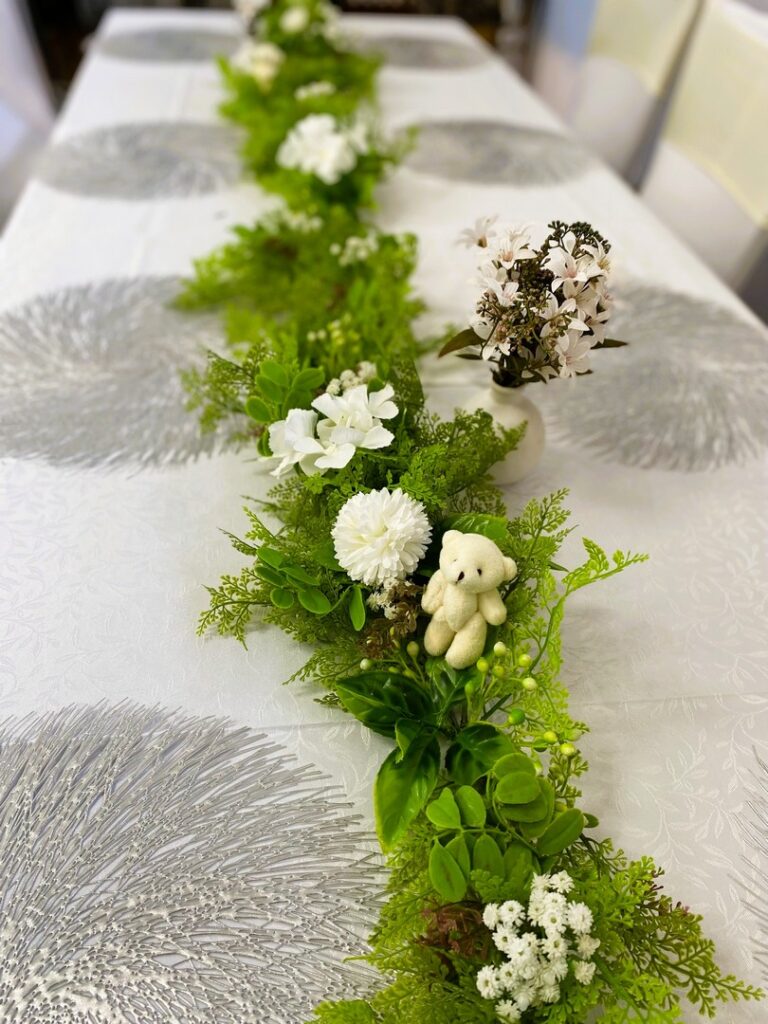 Table centerpiece with green foliage, white florals, and teddy bear decor by Saraya D Decor Adelaide